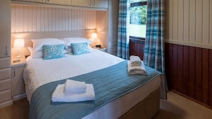 A neatly made bed with a blue quilt, two pillows with a floral pattern, and a folded towel on the bed. - Birch Lodge 19 with Hot Tub (Newton Stewart)