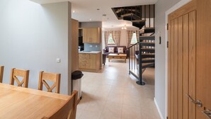A modern kitchen with wooden cabinets, a dining area with a wooden table and chairs, and a staircase leading to an upper level. - Lord Galloway 35 (Newton Stewart)