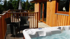 A wooden deck with outdoor furniture, a hot tub, and a building with a window. - Lord Galloway 35 (Newton Stewart)