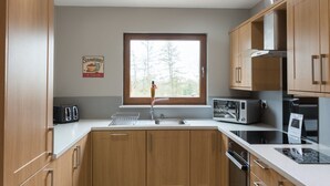A modern kitchen with wooden cabinets, a stainless steel range hood, a microwave, and a built-in oven. - Lord Galloway 35 (Newton Stewart)