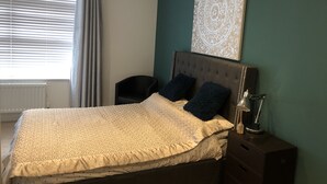 Un lit bien fait, recouvert d’une couvre-lit à motifs, une tête de lit agrémentée de deux oreillers, une table de chevet avec une lampe et une œuvre d’art accrochée au mur.