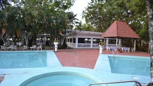 A pool area with two pools, a gazebo, and a covered seating area with chairs and tables. - Hotel La Isla (Parrita)