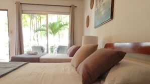 A hotel room with a bed, a window with curtains, a painting on the wall, and a view of palm trees outside. - Hotel La Isla (Parrita)