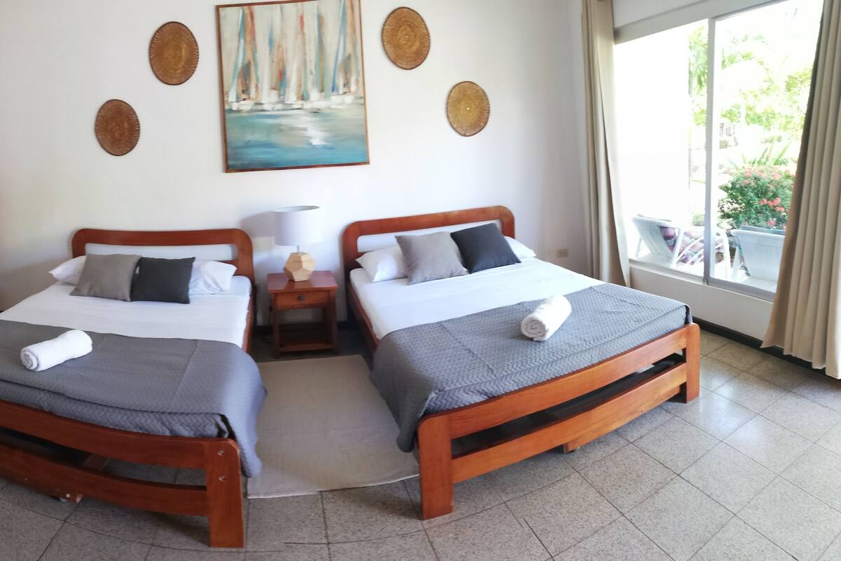 Una habitación de hotel con dos camas de madera, un cuadro en la pared y una ventana con vista a follaje.