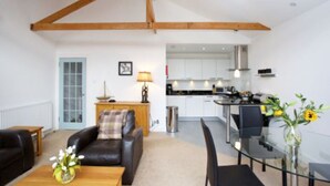 A modern living room with a leather sofa, a glass coffee table, and a dining area with a glass table and chairs. There is a kitchen visible in the background with white cabinets and stainless steel appliances. - Taymouth Marina - Beinn Ghlas (Aberfeldy)