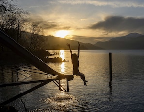 Eine Person springt bei Sonnenuntergang vom Tauchbrett ins Seebecken und macht einen Salto rückwärts.