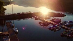 Un port de plaisance avec des bateaux amarrés, une jetée s’avançant dans une eau calme et des montagnes en arrière-plan.