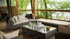 Un espace extérieur aménagé, abrité et doté de mobilier en osier, d’une table basse en verre et offrant une vue sur les arbres.