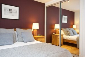 A hotel room with a bed, two bedside tables with lamps, a mirror, and a framed picture on the wall.
