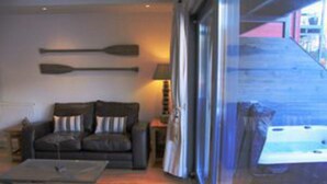 A modern living room with a sofa, a coffee table, and a lamp. There is a large window with curtains, and a view of the outside. - Taymouth Marina - Ben Hope (Aberfeldy)
