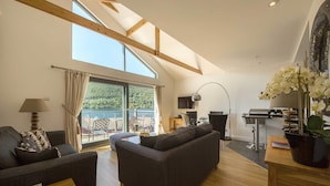 A spacious living room with a high ceiling, a large window, a sofa, a table, and a potted plant. - Ben Lawers (Aberfeldy)