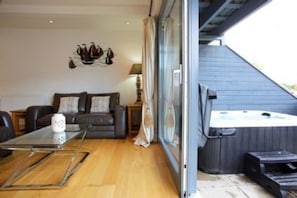Een gezellige woonkamer met een leren bank, een glazen salontafel en een kunstwerk aan de muur. Een schuifpui leidt naar een balkon met een jacuzzi.
