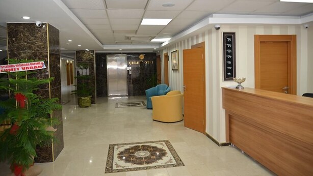 A hotel lobby with a reception desk, a blue armchair, a patterned carpet, and a sign on the wall. - Hasan Celebi Otel (Siverek)