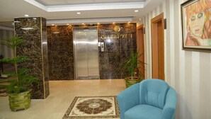 A hotel lobby with a marble reception desk, an elevator, a blue armchair, and a patterned rug. - Hasan Celebi Otel (Siverek)