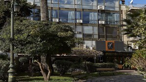 A modern building with large windows, a palm tree in front, and a paved walkway. - Great Living Apartments (Athens)