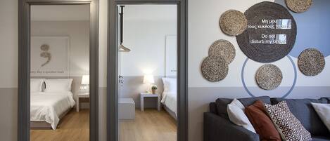 A modern hotel room with a bed, bedside tables, a grey sofa, and decorative woven circles on the wall.