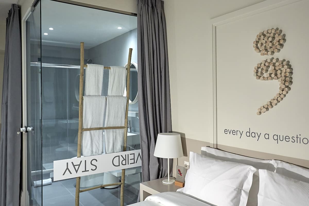 Une chambre d’hôtel comprenant un lit, une table de chevet, une lampe, une œuvre d’art murale et un espace douche.