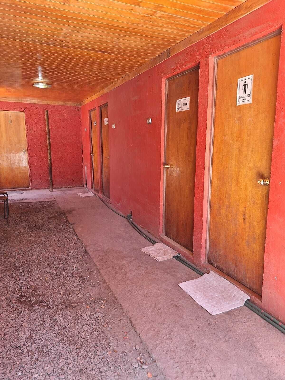 Un couloir aux murs rouges et aux portes en bois, dont certaines sont munies de panneaux indiquant les différents services disponibles.