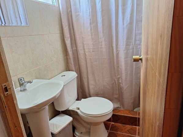 Un baño pequeño con lavamanos, inodoro y cortina de ducha, todo en blanco.