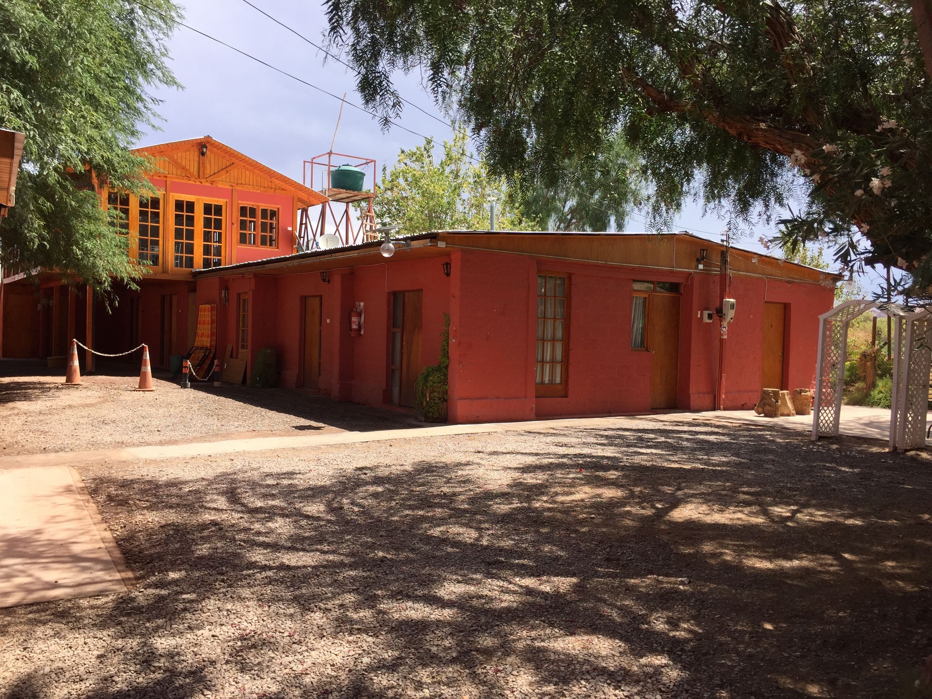 Un edificio rojo con estructura de madera en la parte superior, un área de estar al aire libre cubierta y un jardín vallado.