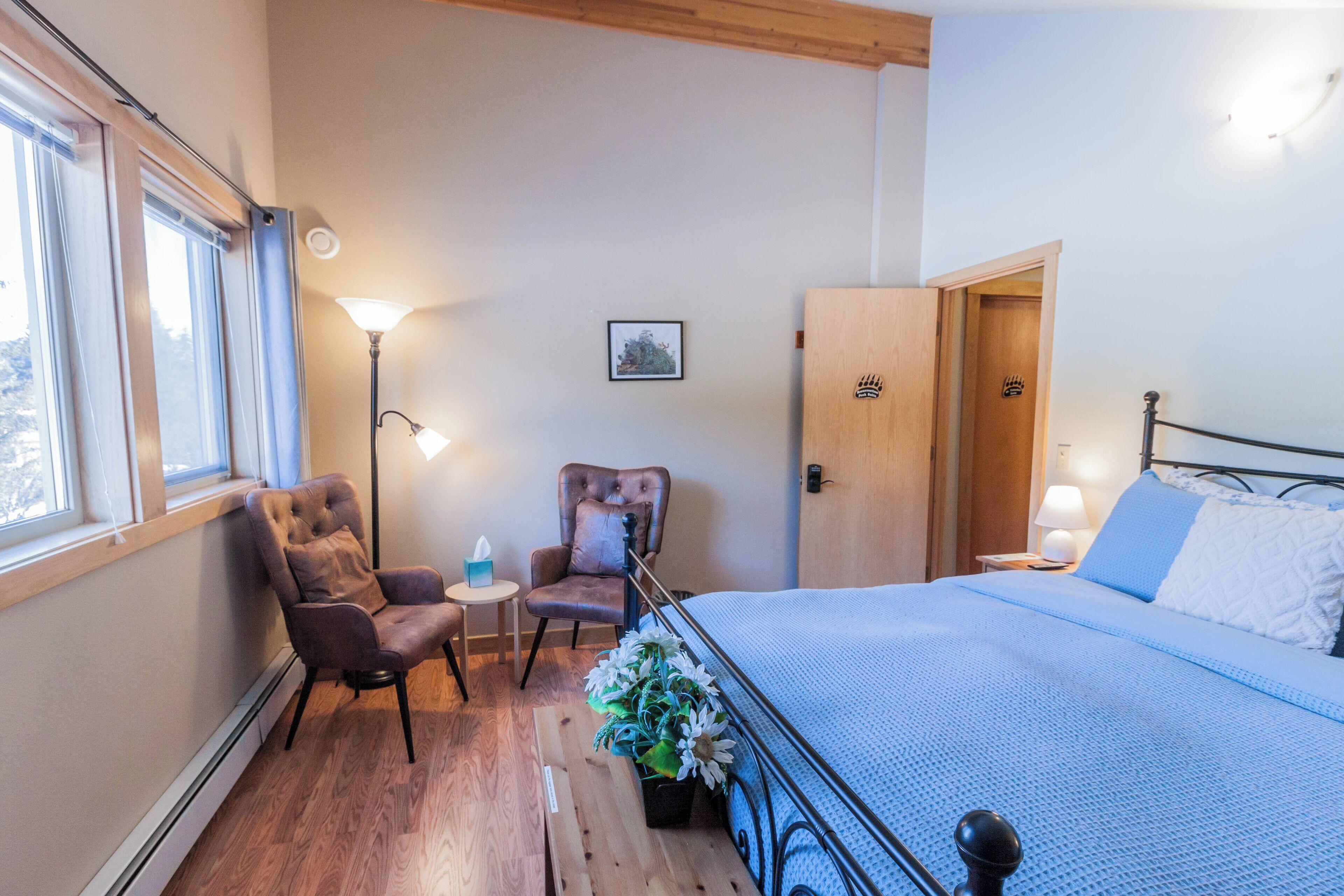 A bedroom with a bed, a chair, a small table, a lamp, and a door.