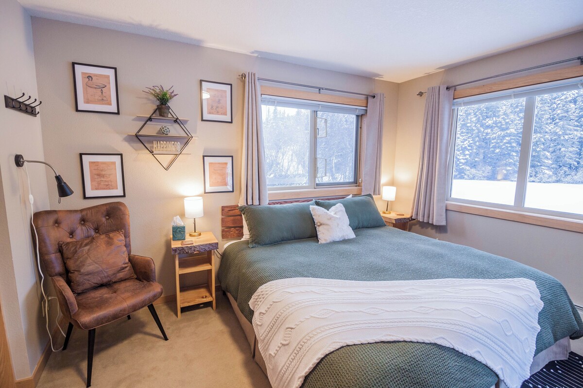 A bedroom with a bed, a chair, a nightstand, and a window with a view of trees.