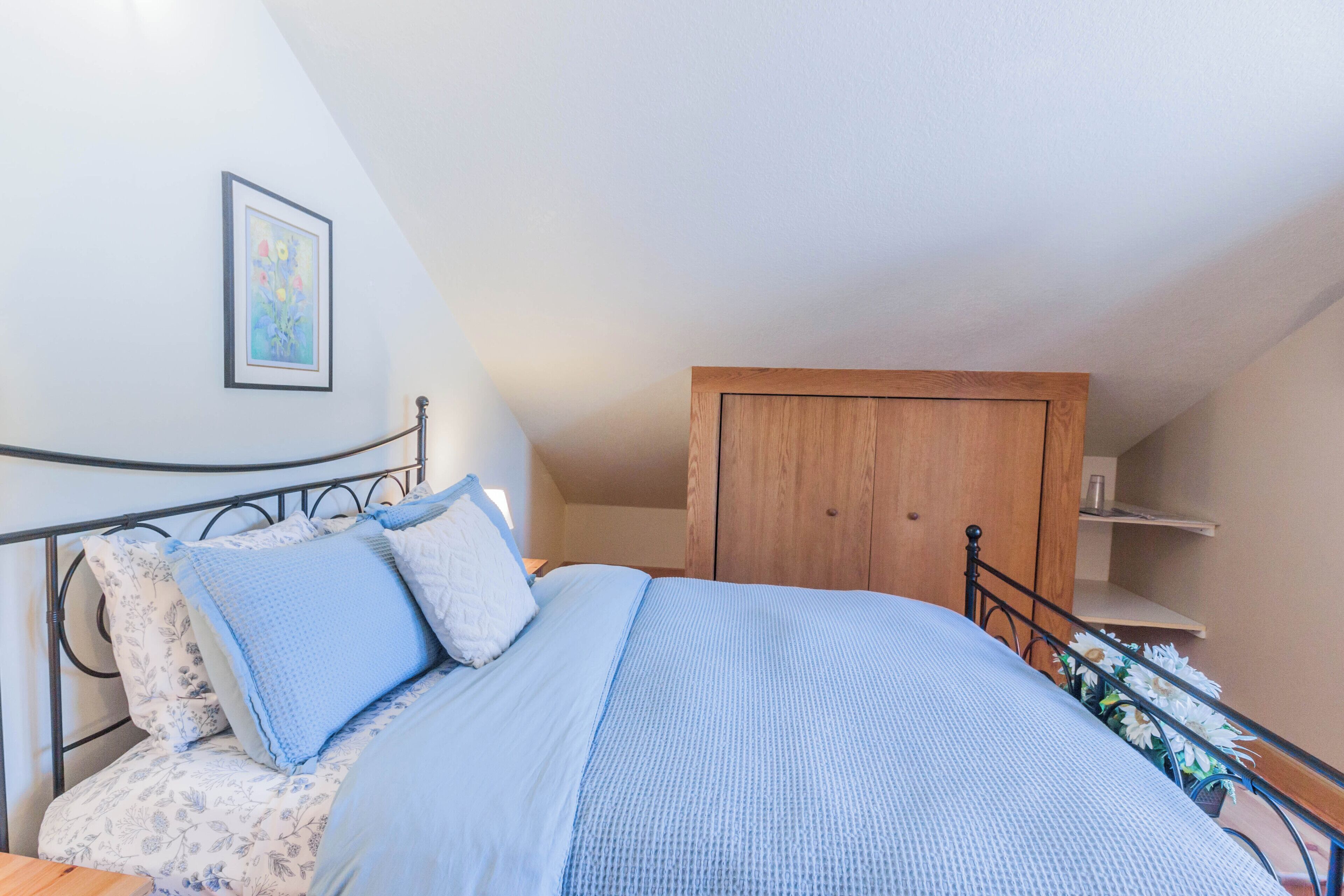 A bedroom with a bed, a wooden wardrobe, and a framed picture on the wall.