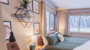 Ein gemütliches Schlafzimmer mit einem Bett, Nachttischen, einer Lampe, einem an der Wand befestigten Regal mit Dekoration und einem Fenster mit Vorhängen.