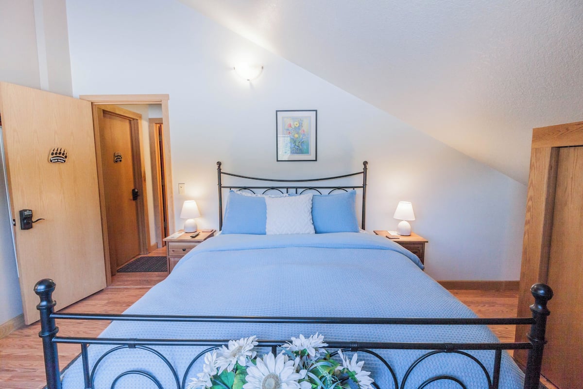 A bedroom with a bed, two bedside tables with lamps, a door, and a framed picture on the wall.