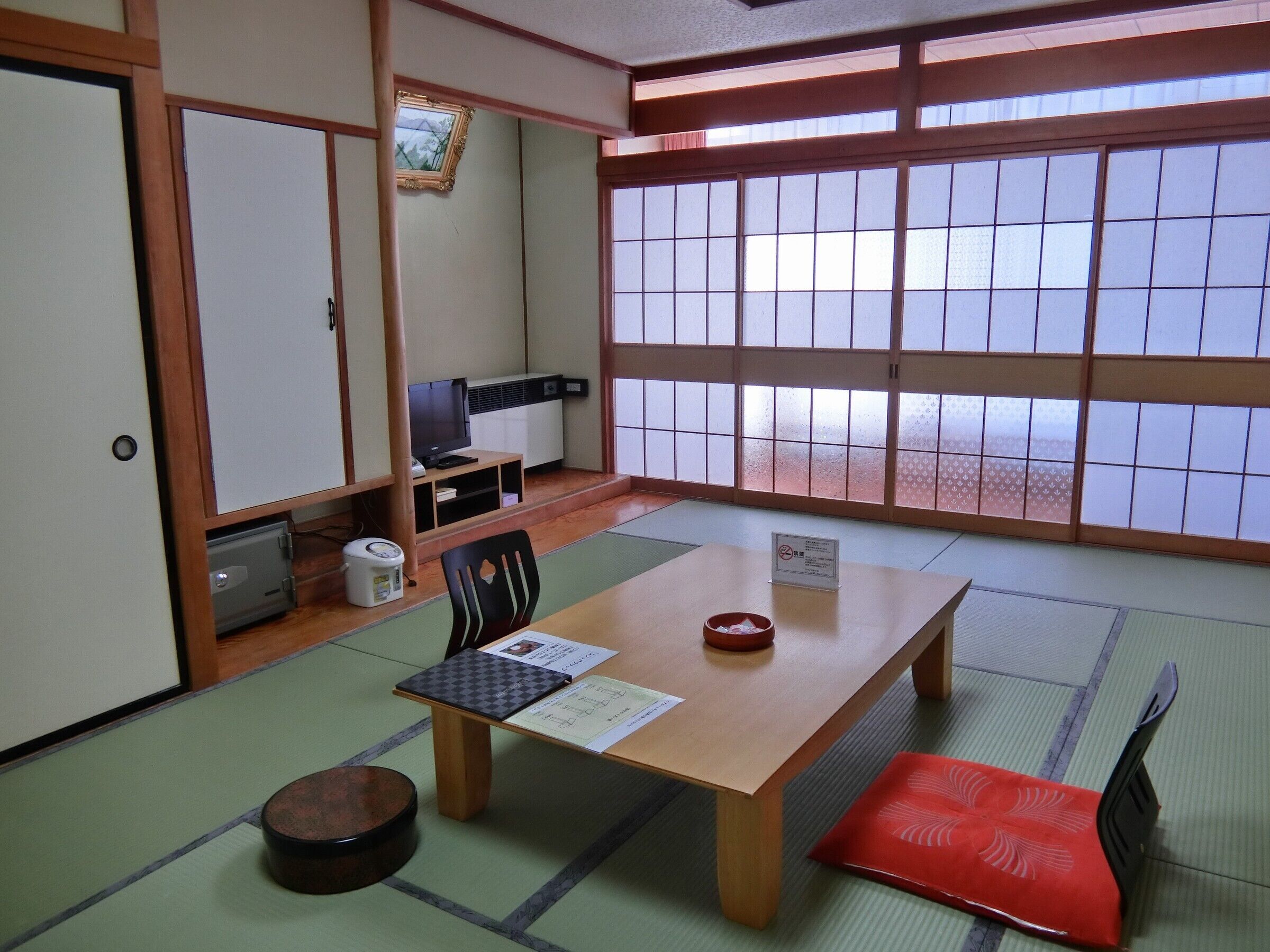 Ein traditioneller japanischer Raum mit Tatami-Böden, einem niedrigen Tisch, einem Fernseher und einer Schiebetür.