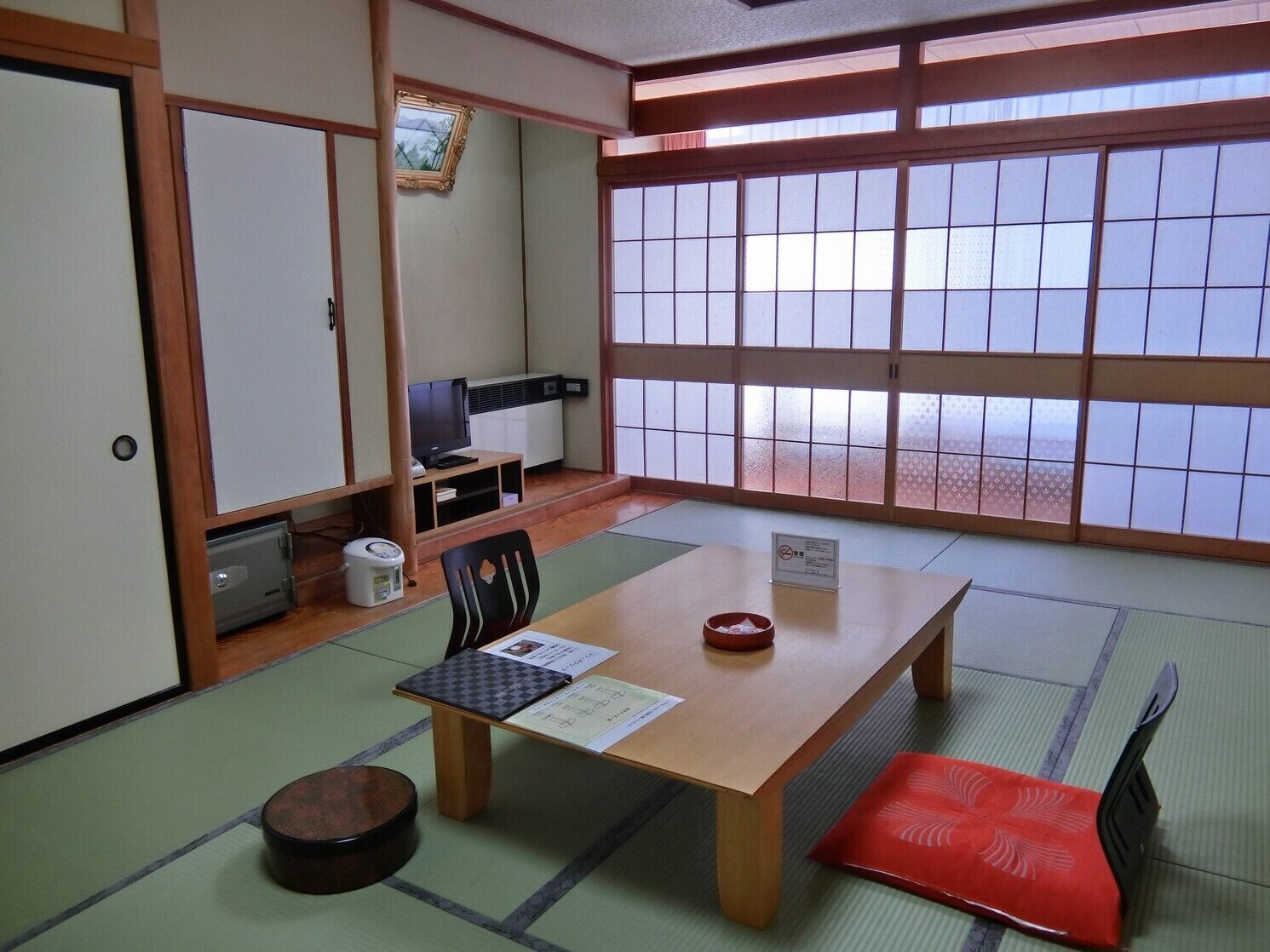A traditional Japanese room with tatami flooring, a low table with a cushion, a television, and a sliding door.