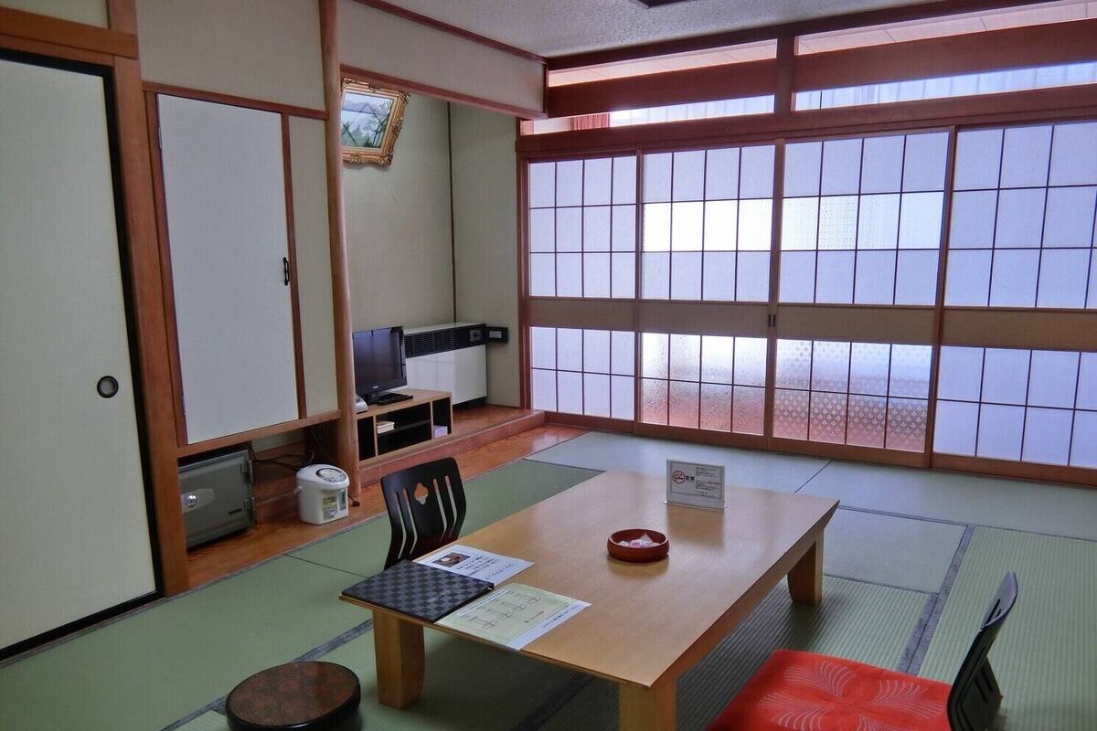 Een traditionele Japanse kamer met tatami vloeren, een lage tafel met kussen, een televisie en een schuifdeur.