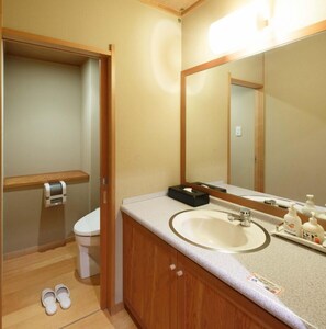 A bathroom with a toilet, sink, mirror, and a pair of slippers on the floor. - Tsutiu Onsen Yamaneya Ryokan (Fukushima)