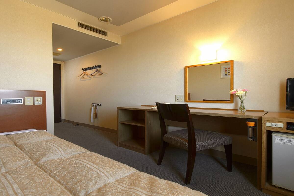 Ett hotellrum med en säng, ett skrivbord, en stol, en tv och ett litet kylskåp.