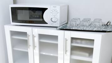A white microwave on a cabinet with a tray of clear glasses.