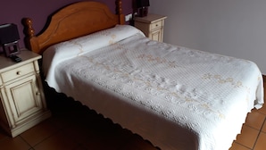 A bed with a wooden headboard, a white bedspread with floral patterns, and a nightstand with a lamp. - Hostal Ardoi (Zizur Mayor)