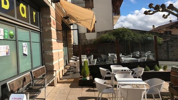An outdoor cafe with tables and chairs, a bar with a sign, and a small garden area. - Hostal Ardoi (Zizur Mayor)