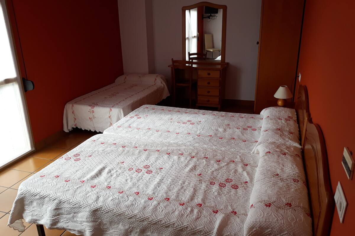 Une chambre avec deux lits simples, une commode en bois, un miroir et une lampe.