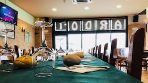 A restaurant with a long table set for dining, a TV screen, and a large window with the word "AROLA" displayed. - Hostal Ardoi (Zizur Mayor)
