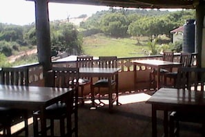 A covered outdoor dining area with wooden tables and chairs, overlooking a lush green landscape. - Paradise Ocean Resort (Moree)