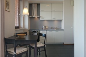 A modern kitchen with white cabinets, a stainless steel range hood, and a dining area with a dark wooden table and chairs. - Chłodna PS Apartments (Warsaw)