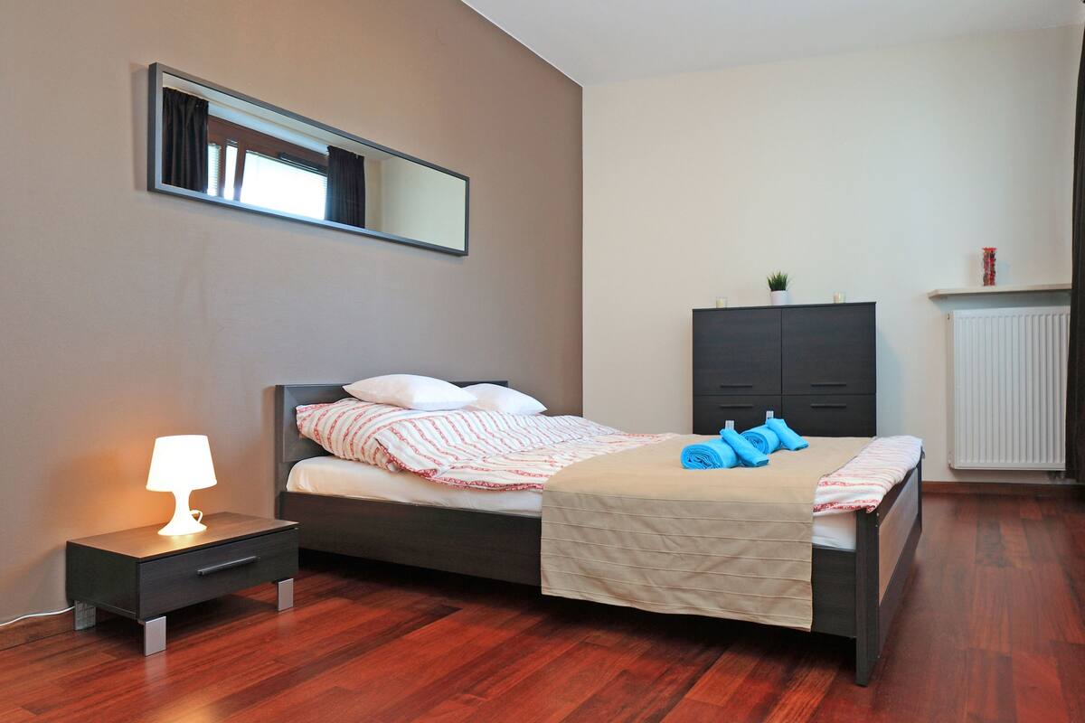 A bedroom with a bed, bedside table, lamp, wardrobe, and a radiator.