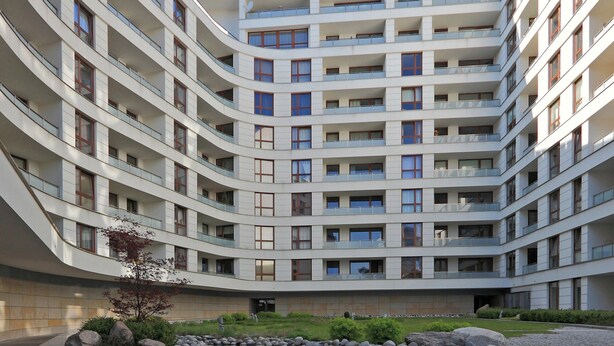 En byggnad med flera våningar och en böjd fasad, en central innergård med en liten damm och en omgivande terräng med stenar.