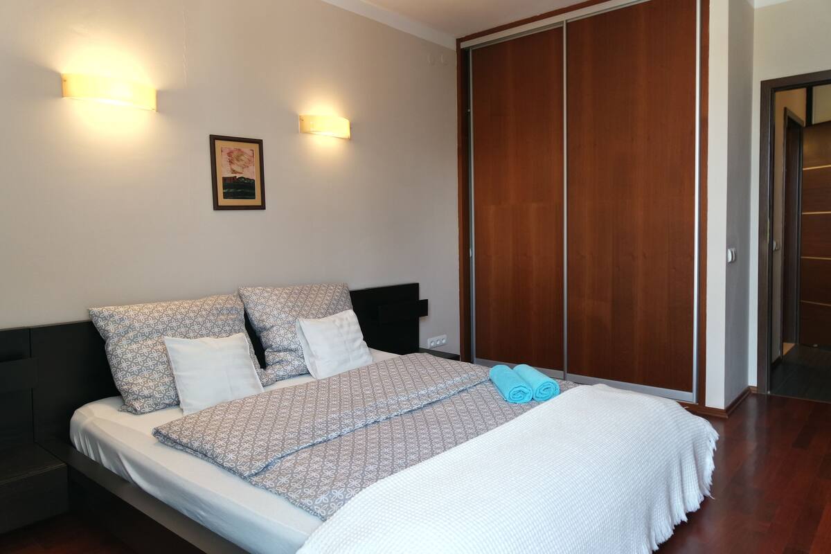 A neatly made bed with patterned bedding, a bedside table, and a wall-mounted light fixture.