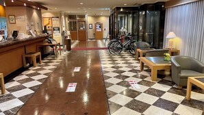 A hotel lobby with a checkered floor, a reception desk, seating area, and bicycles.