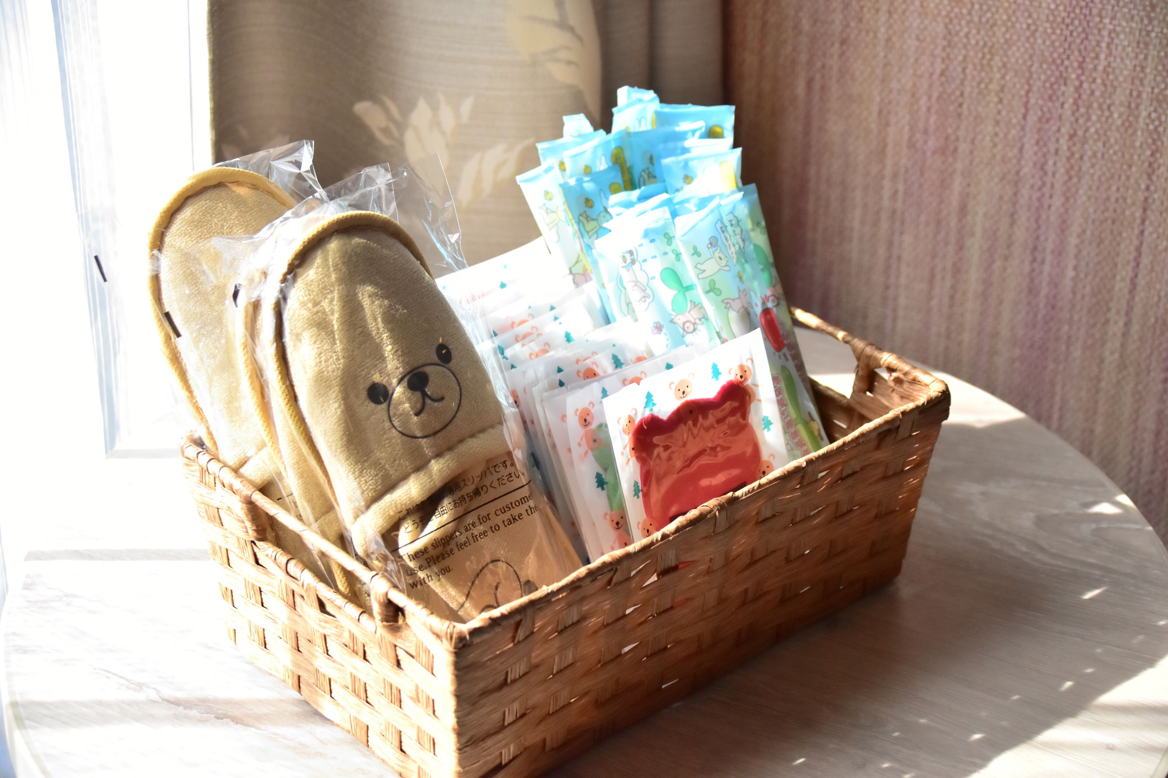 A wicker basket containing a pair of slippers, a teddy bear, and several colorful cards.