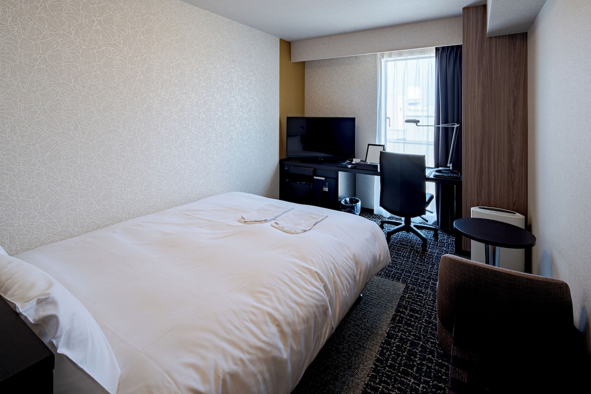Habitación de hotel con una cama grande, un escritorio con computadora, una silla y un televisor.