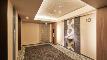 A hotel hallway with a patterned carpet, a ceiling with recessed lighting, and a wall with a number sign.