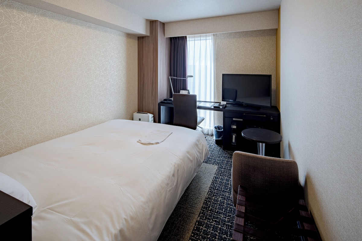 Habitación de hotel con una cama grande, un escritorio con computadora, un televisor y una silla.