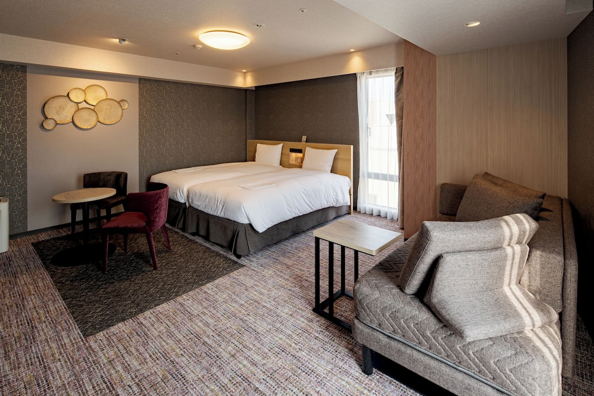 Una habitación de hotel moderna con una cama grande, un sofá, una mesita y una silla.